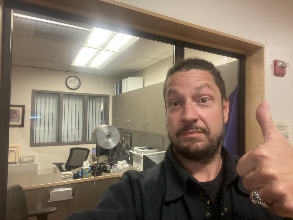 Travis Mateer gives the thumbs up to the camera at the office window of the Missoula Police Department