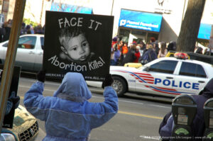 A pro-life demonstrator holds a sign reading “Face It, Abortion Kills!” outside a Planned Parenthood clinic