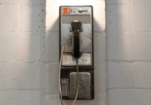 A classic payphone mounted on a white brick wall under a stylish industrial light.