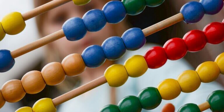 Close-up of colorful wooden abacus with a child learning math in the background, focusing on education and early childhood development.
