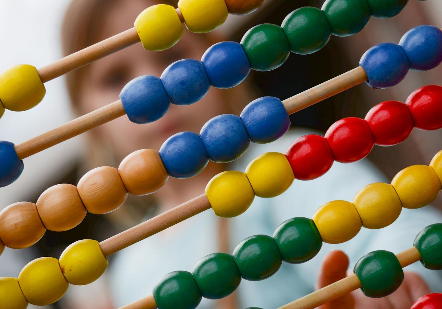 Close-up of colorful wooden abacus with a child learning math in the background, focusing on education and early childhood development.