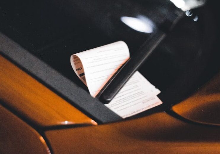 Photo by Erik Mclean Close-up of a parking ticket on a car windshield at night, highlighting urban parking issues.