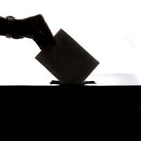 Photo by Element5 Digital Silhouette of a hand placing a vote into a ballot box, symbolizing democracy.