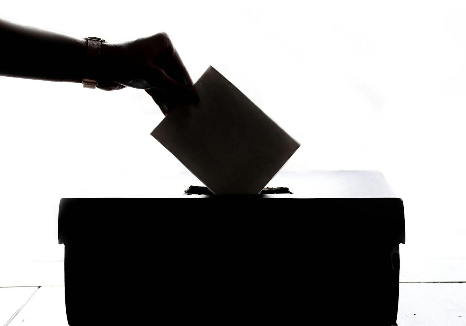 Silhouette of a hand placing a vote into a ballot box, symbolizing democracy.