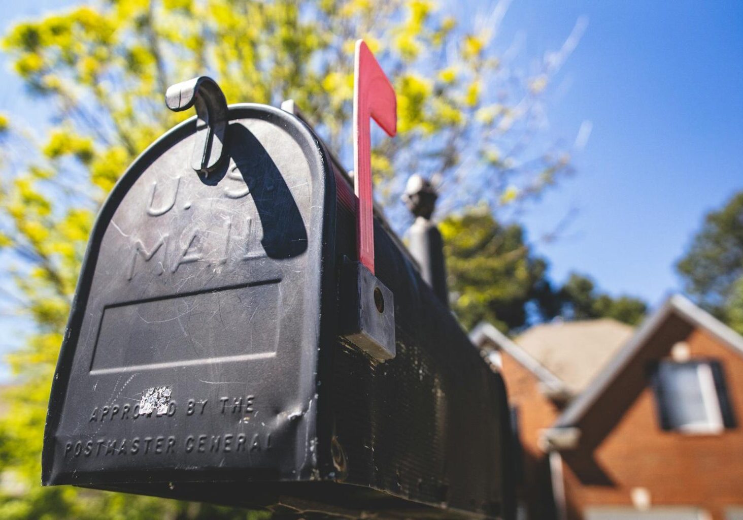 Close-up of a traditional US mailbox with a red flag in a sunny neighborhood.