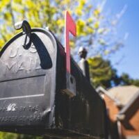 Photo by Abstrakt Xxcellence Studios Close-up of a traditional US mailbox with a red flag in a sunny neighborhood.