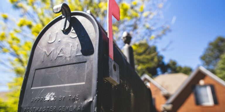 Close-up of a traditional US mailbox with a red flag in a sunny neighborhood.