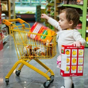 Photo by David Veksler toddle carrying red and white box standing beside yellow shopping cart