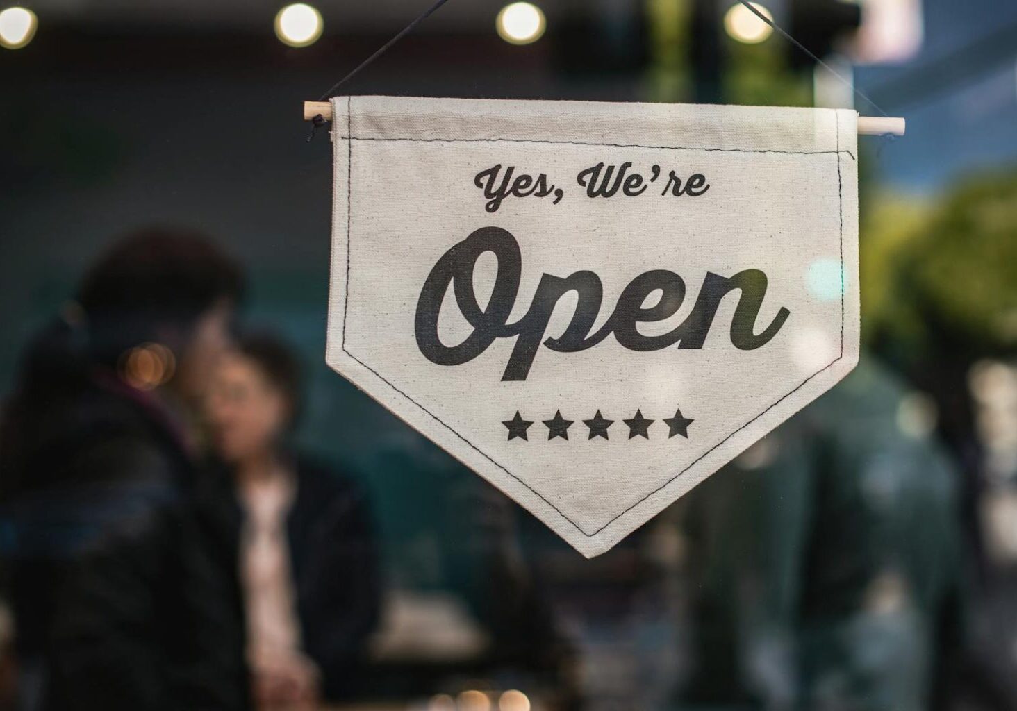 Welcoming open sign displayed in a shop window with blurred background.
