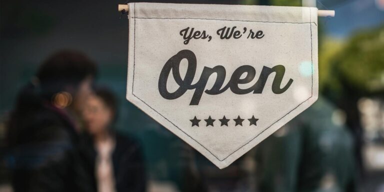 Welcoming open sign displayed in a shop window with blurred background.