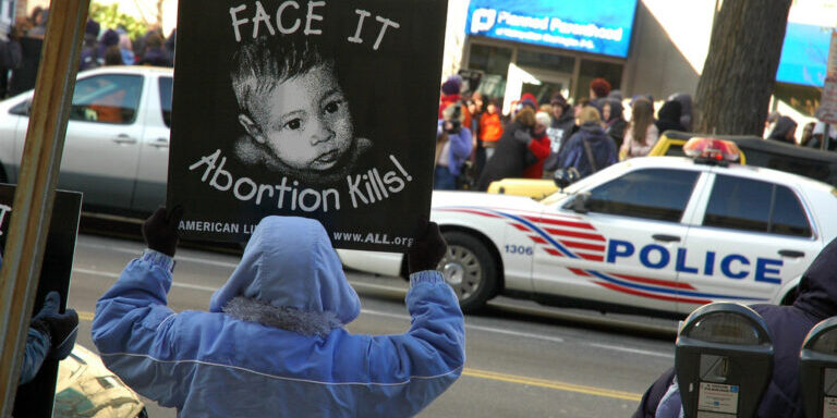 A pro-life demonstrator holds a sign reading “Face It, Abortion Kills!” outside a Planned Parenthood clinic