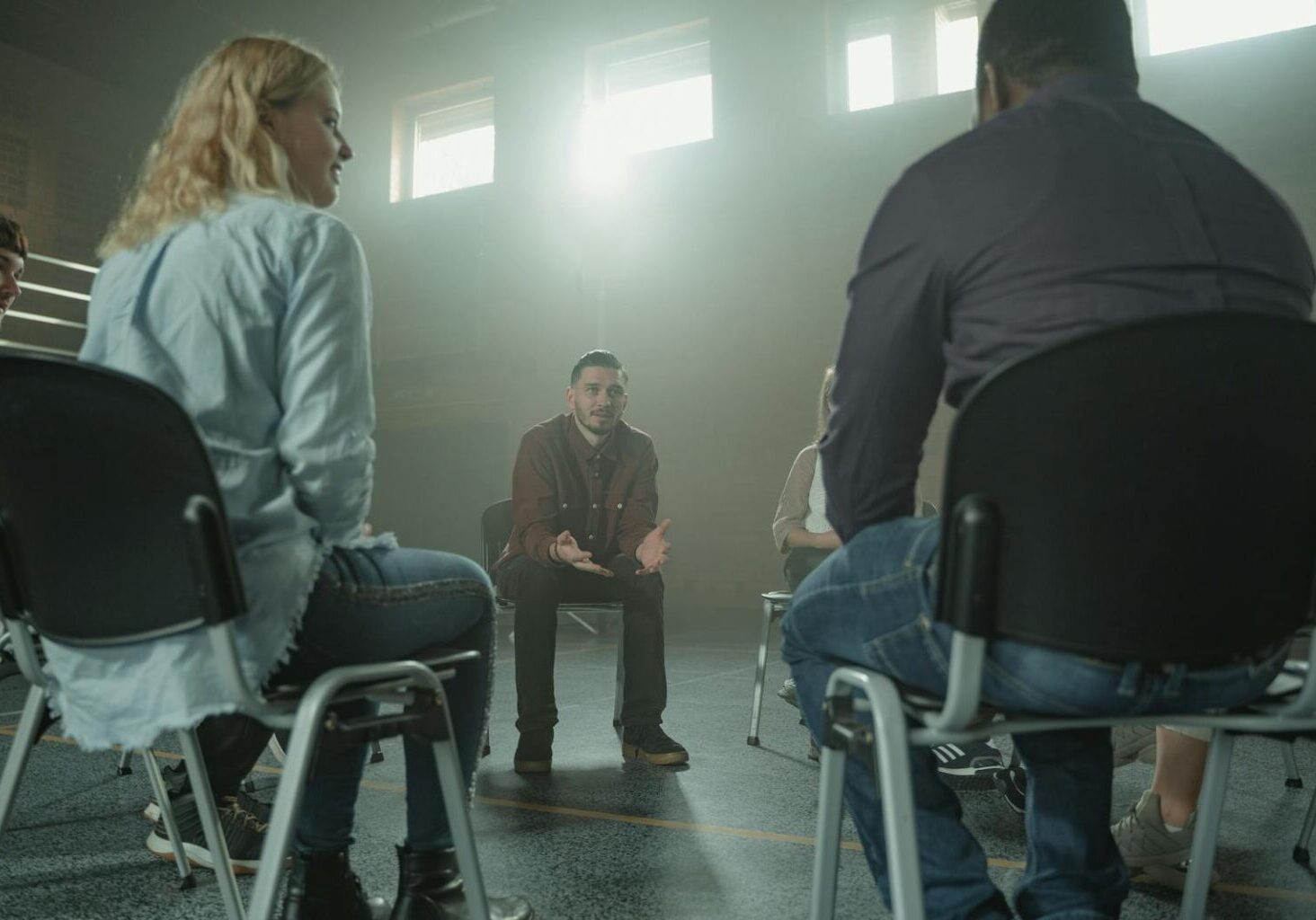 A diverse group of adults in a supportive discussion setting indoors with sunrays.