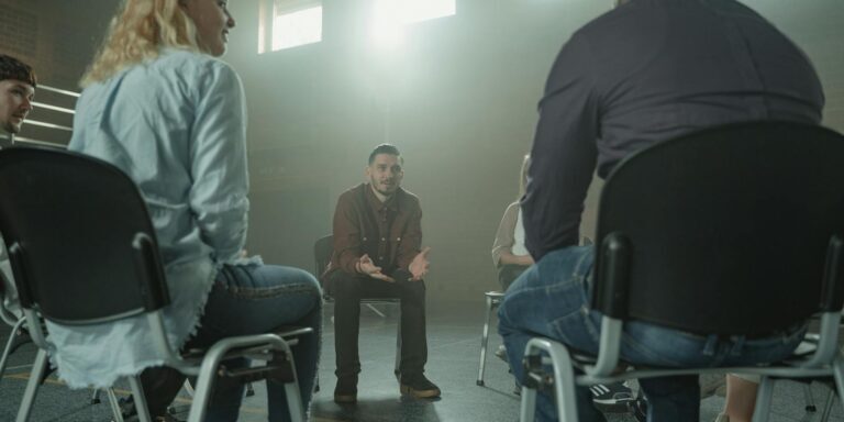 A diverse group of adults in a supportive discussion setting indoors with sunrays.