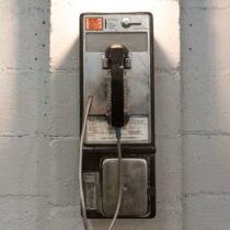 A classic payphone mounted on a white brick wall under a stylish industrial light.