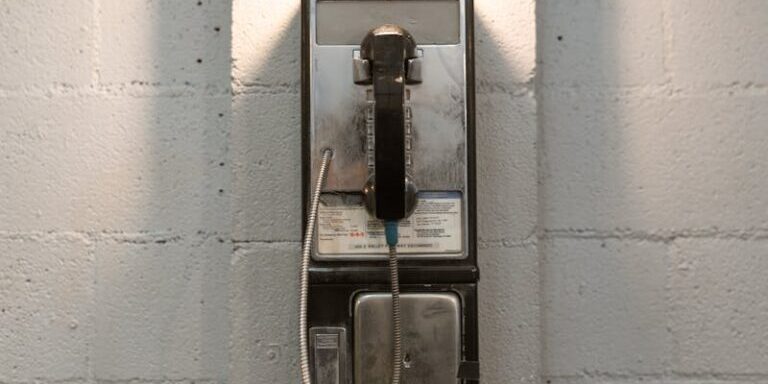 A classic payphone mounted on a white brick wall under a stylish industrial light.