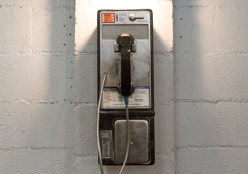 A classic payphone mounted on a white brick wall under a stylish industrial light.