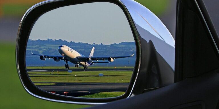 A jet airplane taking off is reflected in a car's side mirror, capturing a unique aviation perspective.
