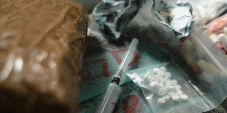 A dramatic scene depicting drugs and syringes on a dark surface, highlighting substance abuse risks.