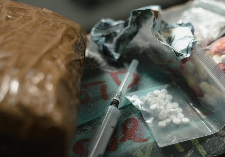 A dramatic scene depicting drugs and syringes on a dark surface, highlighting substance abuse risks.