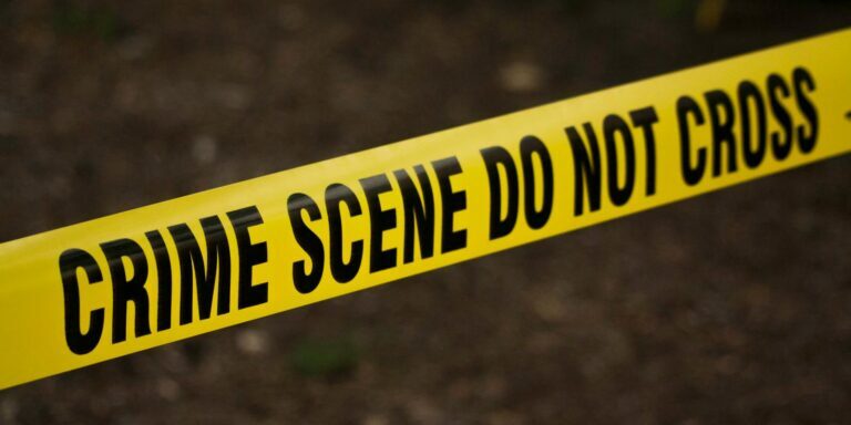 Close-up of crime scene tape with 'Do Not Cross' text, outdoors setting.