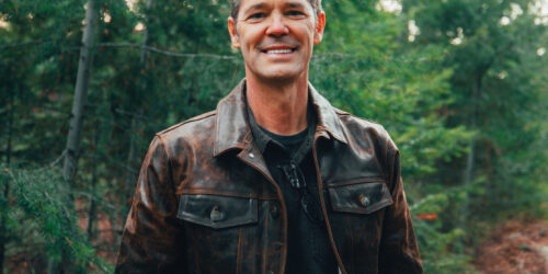 Smiling Man in Leather Jacket Amidst Forest