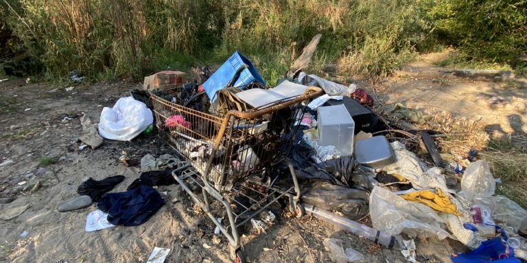 A shopping cart filled with trash surrounded by more trash near the Clark Fork River waterfront