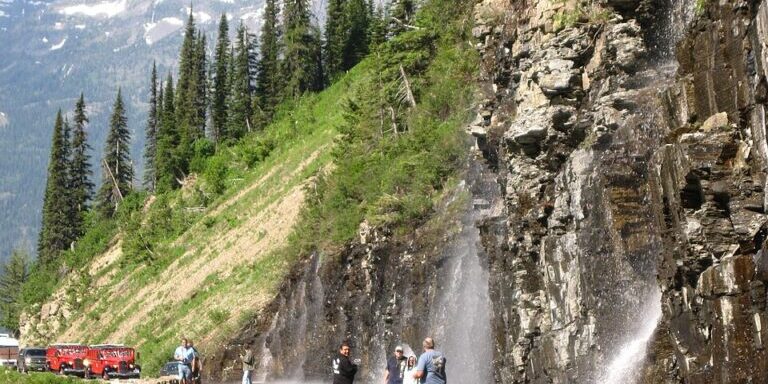 Alpine Cliff Waterfall Sprays Across Mountain Road