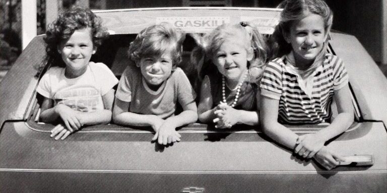 Four children look on from the back window of a Chevrolet station wagon. Coastwatch Magazine. 1979.