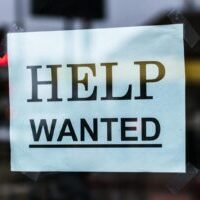Close-up of a Help Wanted sign taped to a glass window in a storefront.