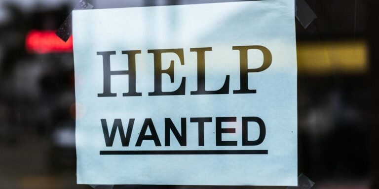 Close-up of a Help Wanted sign taped to a glass window in a storefront.