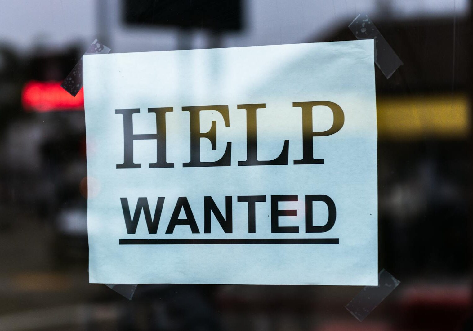 Close-up of a Help Wanted sign taped to a glass window in a storefront.