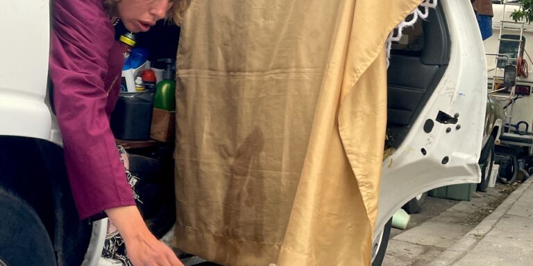 Person leans from the back seat of a car at Hawthorne and Pine behind the Poverello Center to adjust cooking foil on portable camping burner.