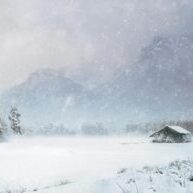 Photo by Simon Berger Serene winter landscape featuring a snow-covered cabin amidst mountains and trees.