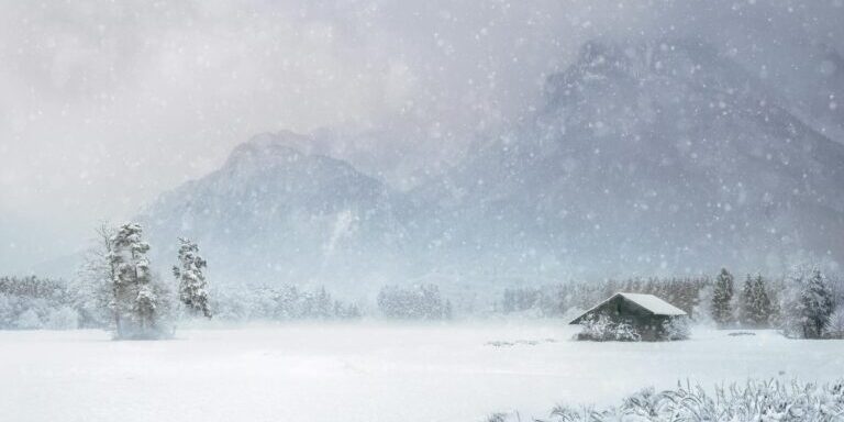 Serene winter landscape featuring a snow-covered cabin amidst mountains and trees.