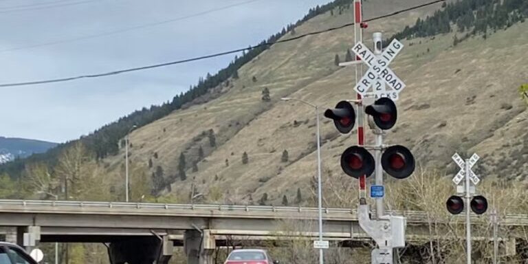 Rural Railroad Crossing with Traffic and Mountain Backdrop
