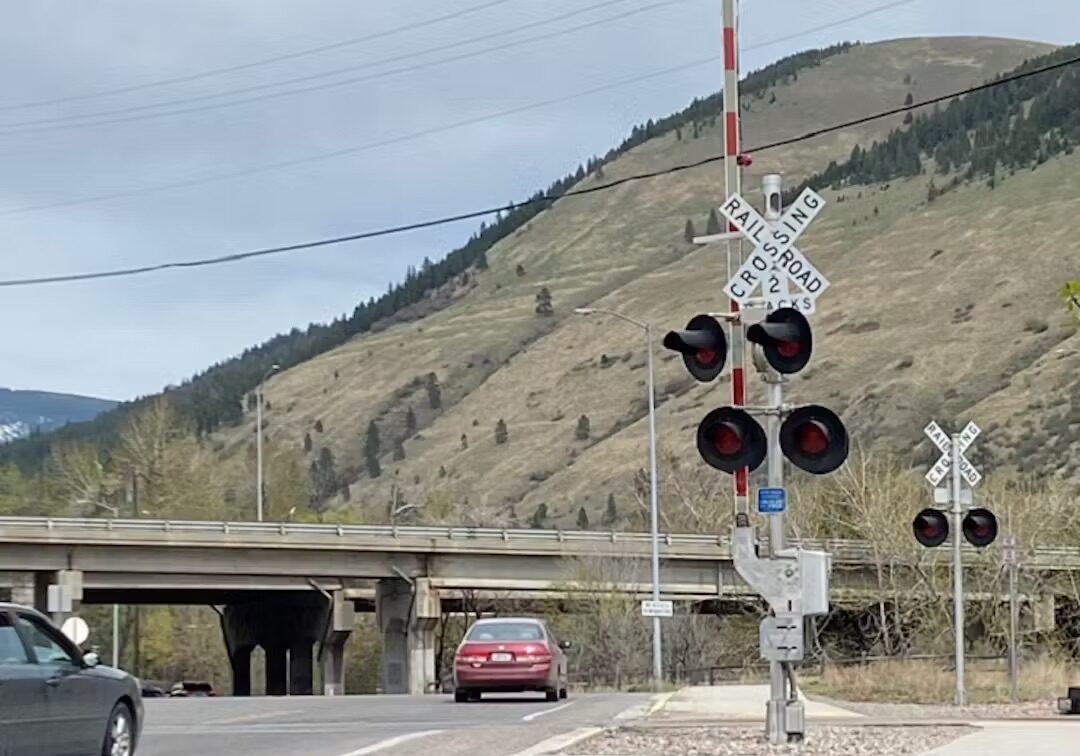Rural Railroad Crossing with Traffic and Mountain Backdrop