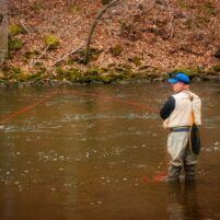 Photo by Paul Wolke woman in brown jacket and brown skirt fishing on river during daytime