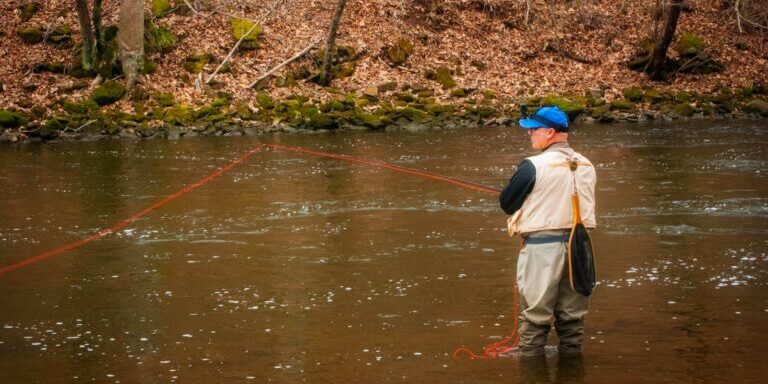woman in brown jacket and brown skirt fishing on river during daytime