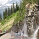 Alpine Cliff Waterfall Sprays Across Mountain Road